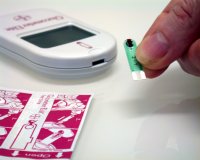 Persona sosteniendo una tira reactiva con una gota de sangre, frente a un medidor de glucosa.